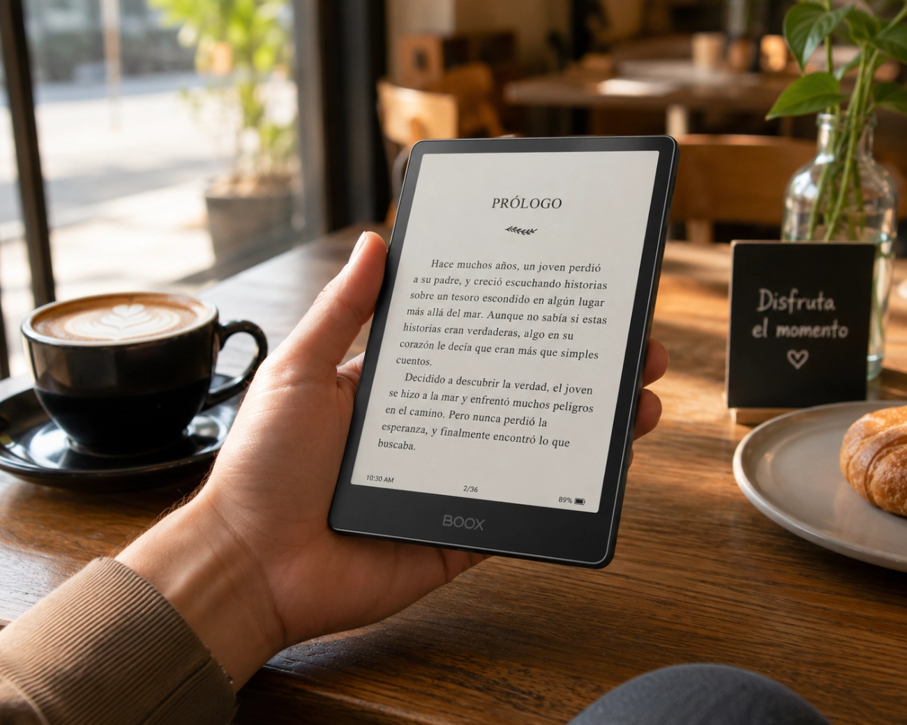En una cafetería, en primer plano una mano sostiene el e-book Boox-Go_6-Gen-II